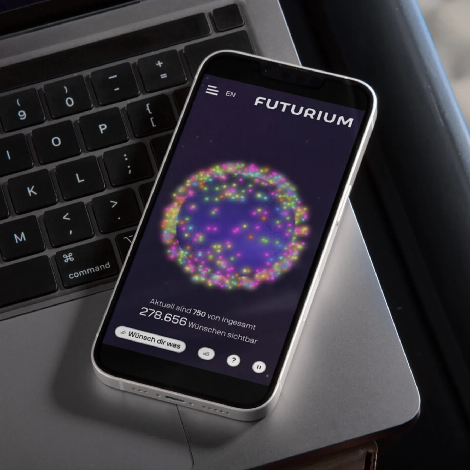 Smartphone mit der Webseite des Futurium auf einer Laptop-Tastatur, zeigt eine bunte, kugelförmige Grafik und Text mit Zahlen zu Wünschen.